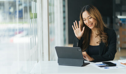 Joyful young woman sit at the work desk, waves hand, greeting colleagues. Attractive business female communicate with colleagues or friends by video call, smiling, remotely work or study