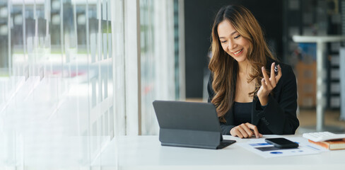 Fototapeta premium Happy young Asian woman sitting at desk at work and using laptop computer for video call