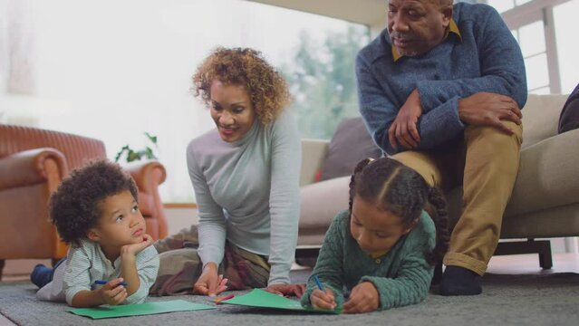 Grandparents sitting on floor at home with grandchildren as they draw picture together - shot in slow motion