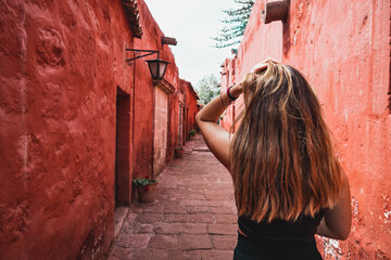 Back view of a caucasian woman touching her hair while walking on a medieval street with red walls.
