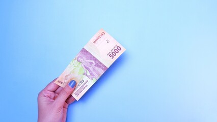 Indonesian Rupiah the official currency of Indonesia. woman's hand is making a payment. Female hand showing Indonesian Rupiah note. Business Investment Economy and Finance concept. Uang 5000 Rupiah.