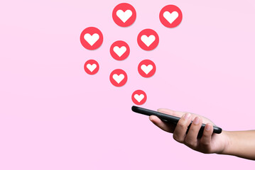 People use mobile phone sending hearts. Love and connection concept using telephone application on pink background.