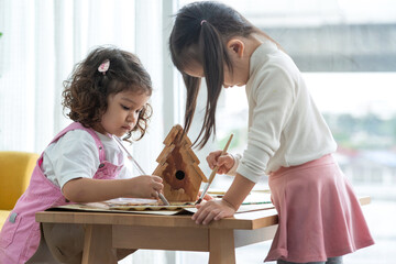 Two little girls help paint a wooden birdhouse in the room, education and learning concept