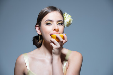 Obraz na płótnie Canvas Sexy summer tropical fruit. Young beautiful model eating orange in studio. Summer mood. Dreaming italian or hispanic girl.