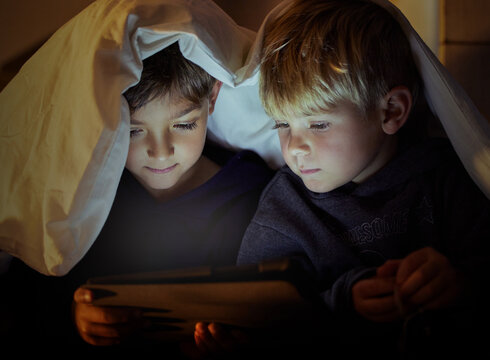 The eyes of children sees everything fresh and full of wonder. Shot of two adorable little boys using a digital tablet under a blanket fort at night in their bedroom.