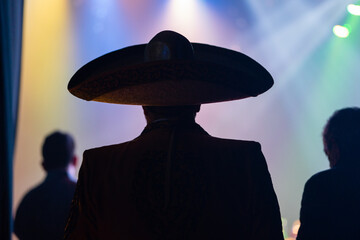 Charro cantante entrando y empezando a cantar y dar su show en un concierto con luces en un escenario musical contraluz sombra con sombrero - obrazy, fototapety, plakaty
