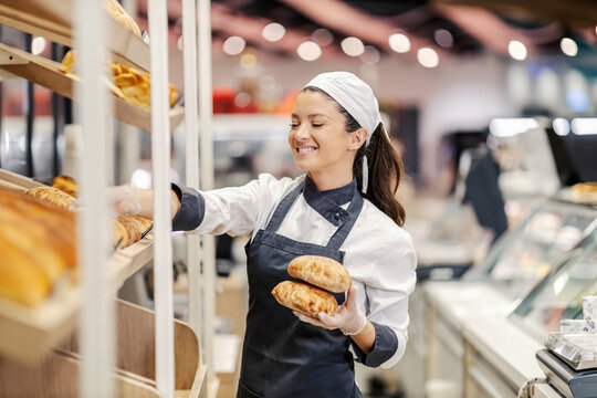 A happy bakery department saleswoman arrange fresh pastry on shelves in supermarket.