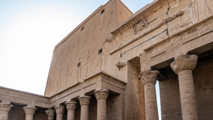 Fototapeta premium A fragment of the temple of Horus in Edfu. Columns with carved capitals, a wall with huge images of gods are visible. Blue sky. Egypt
