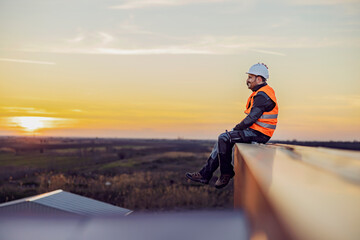 A constructor sitting on the height and smiling. - obrazy, fototapety, plakaty