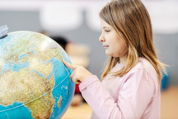 A schoolgirl pointing at the globe at geography class.