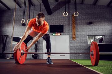 A handsome man sets up a barbell with weights in a modern sports gym.