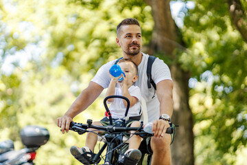 A boy drinks water while father riding a bike in nature.