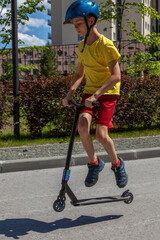 A young man in a yellow T-shirt and a blue helmet rides a stunt scooter through the city.