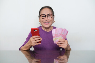 Elderly Asian woman showing happy face when holding mobile phone and money