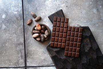 Stack of chocolate bars with cocoa beans. Flat lay composition with delicious chocolate on black background. Space for text