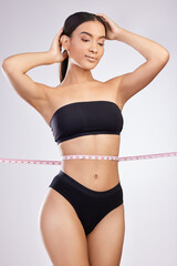 Fototapeta premium Ive finally lost all that stubborn belly fat. Studio shot of a beautiful young woman posing with a tape measure around her waist against a white background.