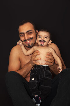 Portrait of a father with a baby with a painted mustache on a black background. High quality photo