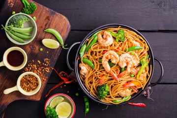 Stir-fried spaghetti or stir-fry noodles with vegetables and shrimp in a black frying pan. dark...