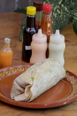 Un primer plano del burrito de tortilla de harina con las salsas en la mesa de madera