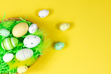 Easter nest with eggs and feathers on a yellow background. View from above. Place for text, lettering. Easter concept.