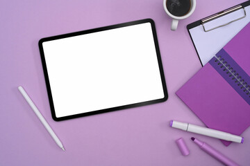 Flat lay digital tablet with empty display, coffee cup and stationery on purple background.