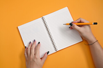 Stylish woman holding pencil and writing on empty notebook.