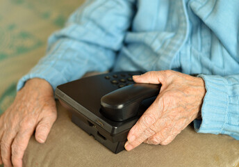 Closeup of pensioner's hands holding a retro push-button landline phone