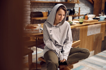 Young desperate woman in hooded shirt thinking of her problems at home.