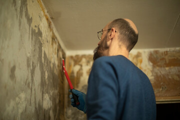 Guy is renovating house. Man removes wallpaper from wall.