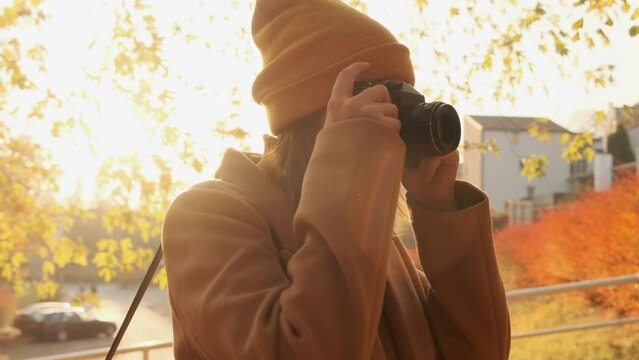 The camera pans around a young woman photographer taking a photo at sunset in an autumn park.