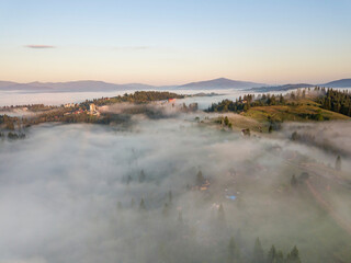 Mountain settlement in the Ukrainian Carpathians in the morning mist. Aerial drone view.