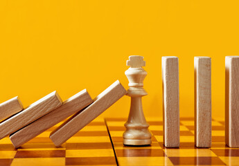 Chess piece king resists and stops the domino effect of the wooden blocks.