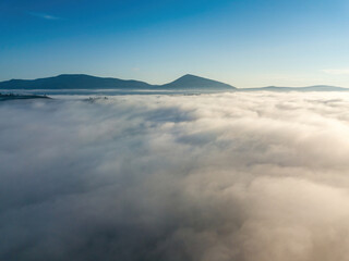 Flight over fog in Ukrainian Carpathians in summer. A thick layer of fog covers the mountains with a solid carpet. Mountains on the horizon. Aerial drone view.
