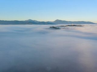 Sunny morning in the foggy Carpathians. A thick layer of fog covers the mountains. Aerial drone view.