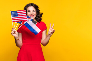 Woman in red dress shows bunch of diverse flags cheerfully smiling at camera over yellow studio...