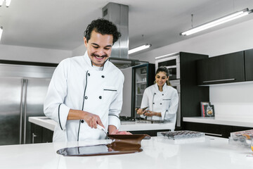 Fototapeta premium hispanic man pastry chef wearing uniform in process of preparing delicious mexican sweets chocolates at kitchen in Mexico Latin America