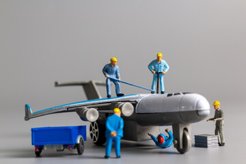 Miniature people worker team checking and repairing airplane on gray background

