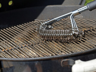 Cleaning a grill, dirty grill grate is cleaned with stainless steel grill brush - obrazy, fototapety, plakaty