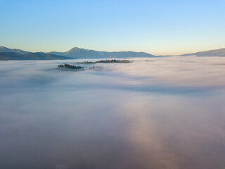 Fototapeta premium Sunny morning in the foggy Carpathians. A thick layer of fog covers the mountains. Aerial drone view.