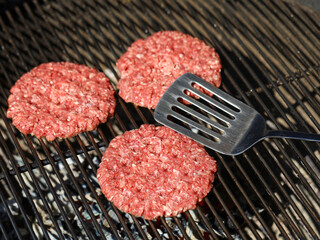 top view of raw beef hamburger patties on barbecue grill grate with spatula
