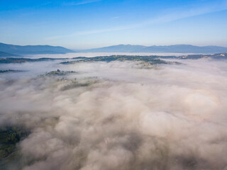 Flight over fog in Ukrainian Carpathians in summer. Mountains on the horizon. Aerial drone view.