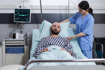 Nurse fixing pillow taking care of patient with respiratory insufficiency connected to vitals...