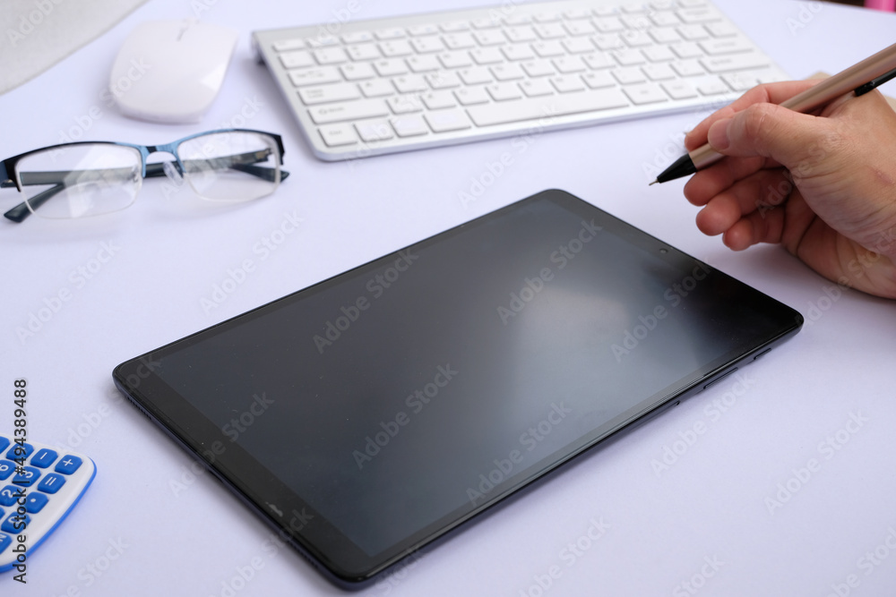 Poster hands holding a tablet computer with an isolated screen and a business desk with a pc, wireless mous