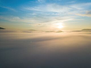 Fototapeta premium The rays of dawn over the fog in the Ukrainian Carpathians. Aerial drone view.