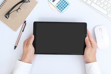 Hands holding a tablet computer with an isolated screen and a business desk with a PC, wireless mouse, and keyboard business-related items