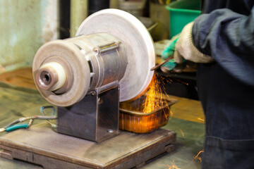 Metal Machining Concepts. Professional Fitter in Protective Gloves and Uniform Using Gringer Tool For Metal Work With Bunch of Sparks in Workshop.