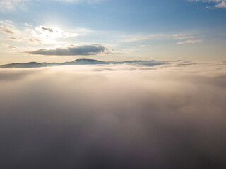 Flight over fog in Ukrainian Carpathians in summer. Mountains on the horizon. A thick layer of fog covers the mountains with a continuous carpet. Aerial drone view.