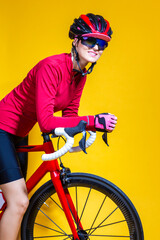 Fototapeta premium Female in Cycling Ideas. Professional Female Road Cyclist Posing With Modern Carbon Race Bike In Long Sleeve Cycling Outfit Against Yellow Background.