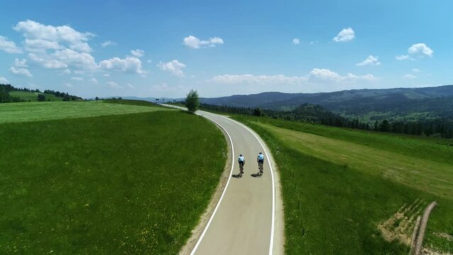 Aerial view of mountain empty road and two bikers cycling. In the background wide mountain range and epic alpine view. Concept: Vacations in the mountains, traveling on a bike