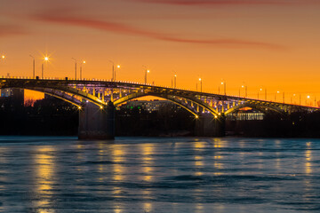 Fototapeta na wymiar Bridge at sunset, with yellow illumination, frozen river, ice.